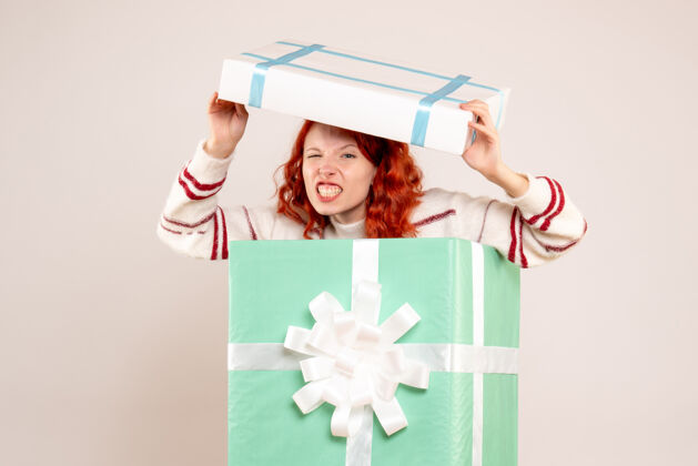 可爱年轻女子隐藏在白色墙上的圣诞礼物内的正面视图节日盒子人