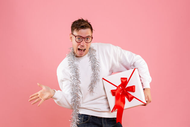 正面一个年轻人在粉红色的墙上拿着圣诞礼物的正面图男性礼品盒快乐