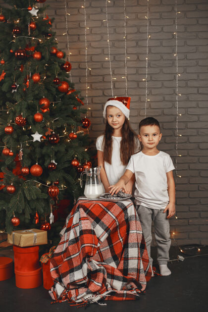 礼物站在圣诞树旁的孩子们吃牛奶饼干的孩子们红色可爱男孩