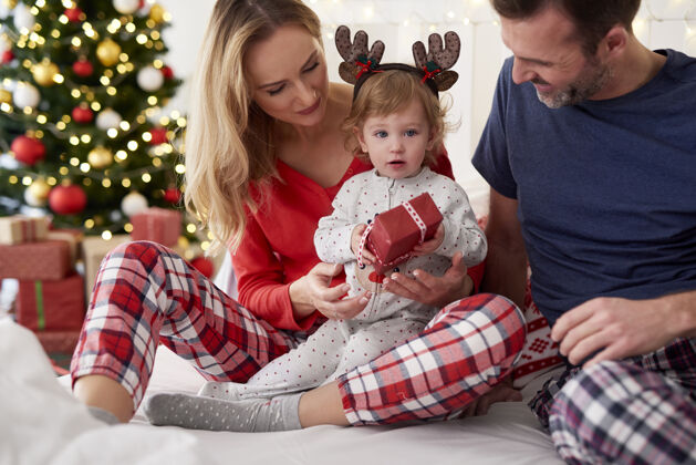 近距离宝宝在床上和父母一起打开圣诞礼物圣诞树女儿舒适