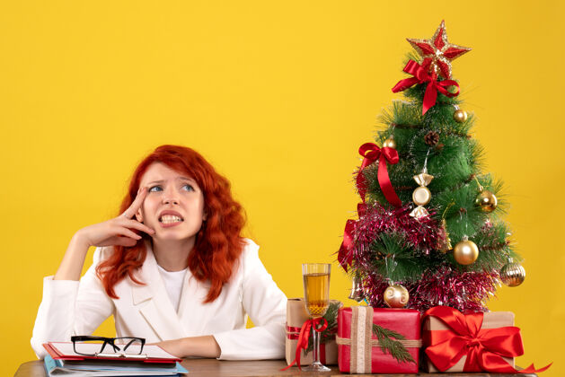 人女工人坐在桌子后面 手里拿着圣诞礼物和黄色的圣诞树礼物工人黄色