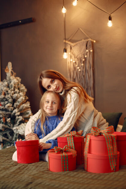 床人们在为圣诞节做准备母亲在和女儿玩耍一家人在节日的房间里休息孩子穿着蓝色毛衣圣诞节杉木闪亮