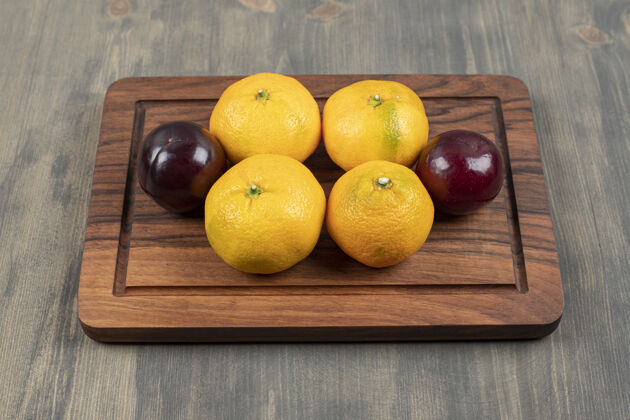 新鲜木砧板上的甜橘子和李子高质量的照片健康柑橘李子