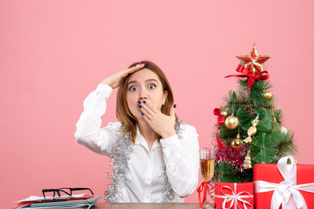 脸女工正坐在桌子后面 手里拿着圣诞礼物 脸上挂着粉色的震惊表情坐着礼物女