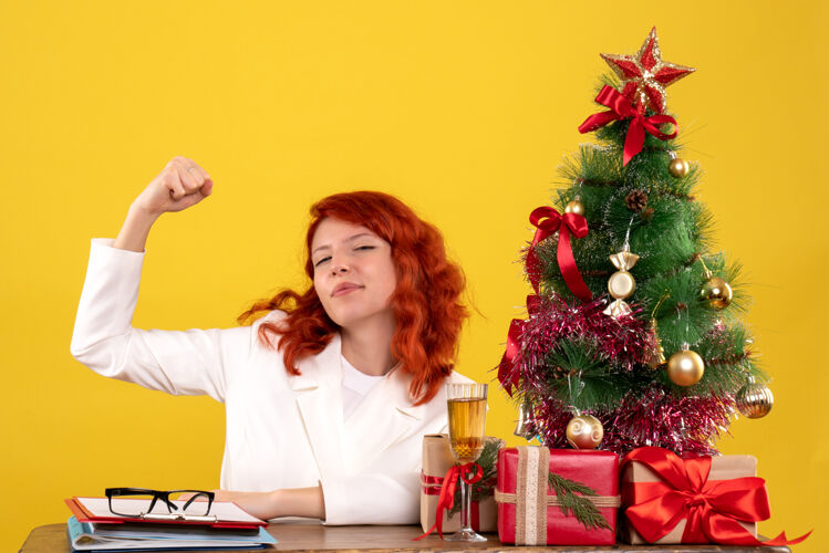 圣诞节女工人坐在桌子后面 拿着圣诞树和黄色的礼物女女工人桌子