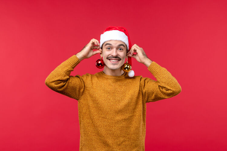 玩具红墙上拿着圣诞树玩具的年轻人的正视图快乐人帽子