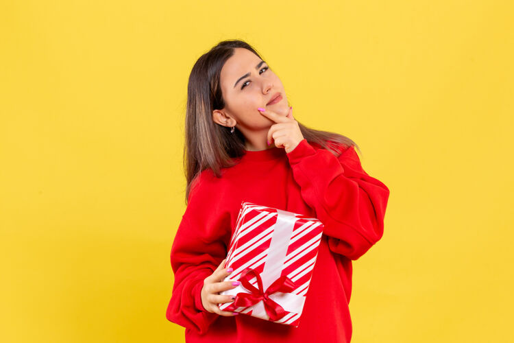 脸黄色墙上年轻女子手持圣诞礼物思考的正面图十二月节日礼物