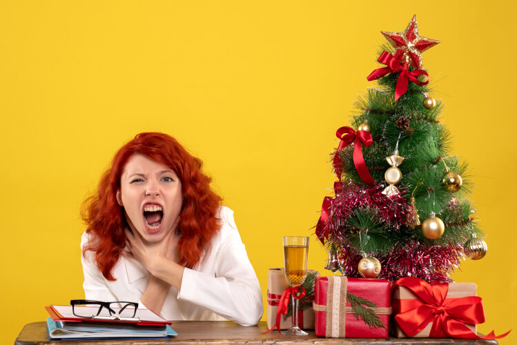 工人女工人坐在桌子后面 手里拿着圣诞礼物和黄色的圣诞树办公室树坐着