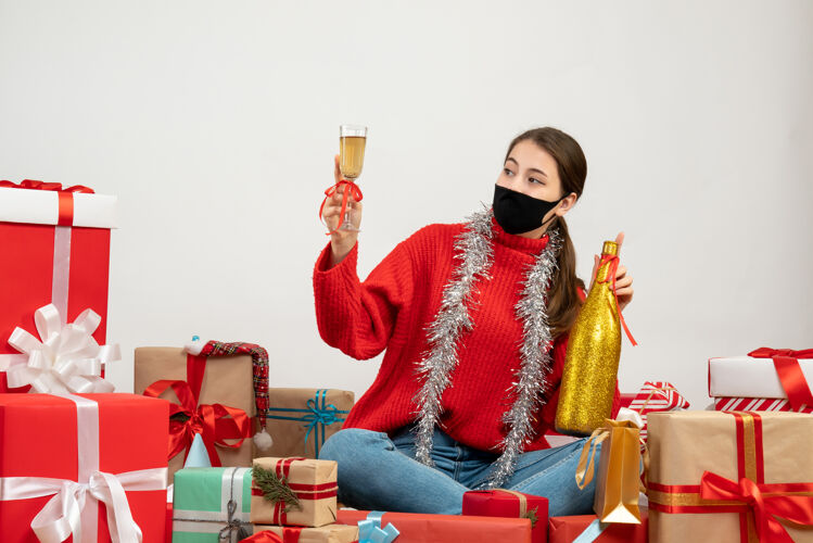 圣诞节戴着黑色面具的派对女孩拿着香槟瓶 围坐在白色的礼物旁敬酒人面具礼物