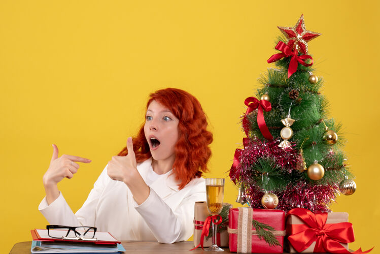办公室女工人坐在桌子后面 拿着圣诞树和黄色的礼物礼物圣诞节坐着