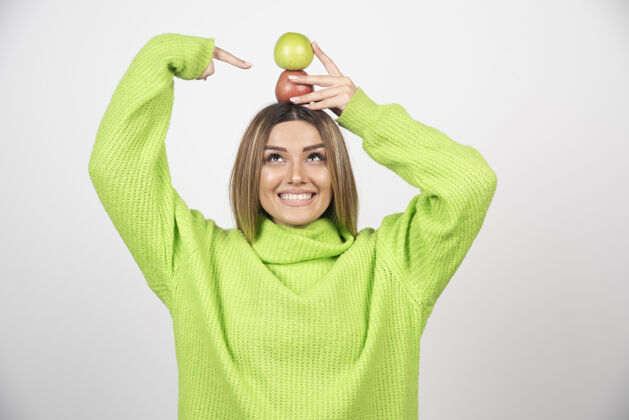 食欲身穿绿色t恤的年轻女子头顶举着两个苹果举行年轻苹果