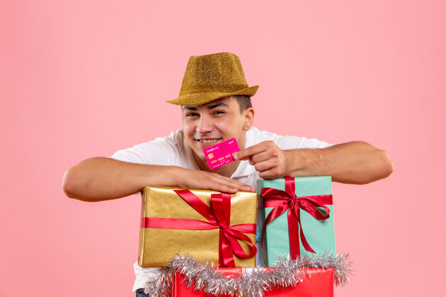 礼品盒年轻人在圣诞节前后的正面图 粉红色的墙上挂着一张银行卡银行快乐男性
