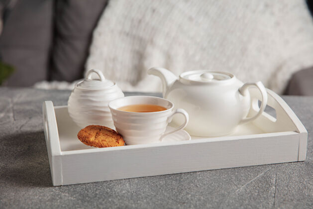 茶白色茶具和蛋糕放在木制的灰色桌子上白色的木制托盘上有杯子 茶壶和花环灯桌子咖啡温暖