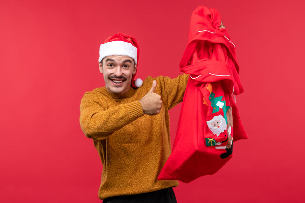 礼物红墙上拿着礼物包的年轻人的正视图服装男性欢乐