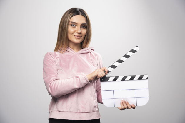 女穿着粉色运动衫的金发女士拿着一块空白的隔板 摆出专业的姿势视频电影拍板