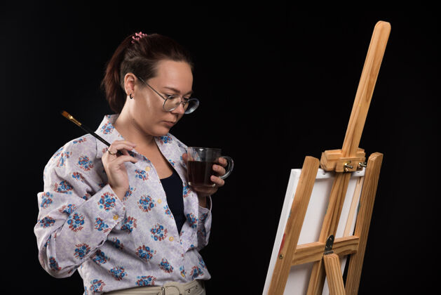艺术女画家拿着画笔 看着黑色背景上的画布黑色绘画工艺