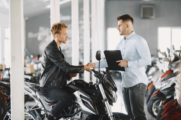 购买男人在摩托店里选摩托车穿黑色夹克的家伙经理和客户在一起消费主义交易展览
