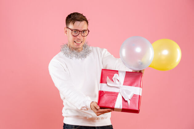 礼品盒手持气球和礼物的年轻人在粉红色墙上的正视图庆祝人快乐