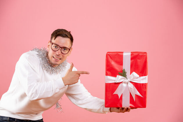 男性在粉红色的墙上年轻人给某人送圣诞礼物的正面图节日圣诞快乐时尚