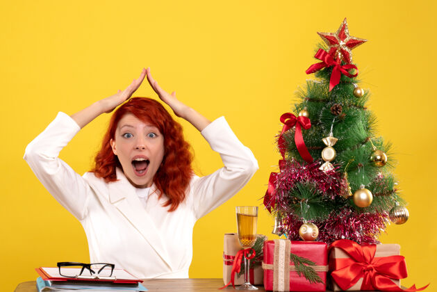 圣诞树女工人坐在桌子后面 手里拿着圣诞礼物和黄色的圣诞树餐桌圣诞节黄色