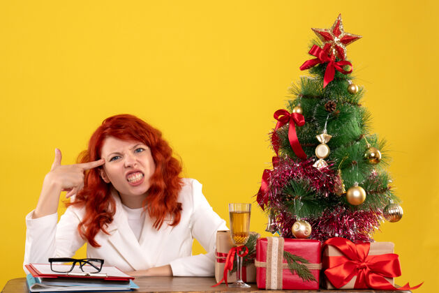 礼物女工人坐在桌子后面 手里拿着圣诞礼物和黄色的圣诞树情感工人树