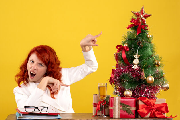 工人女工人坐在桌子后面 手里拿着圣诞礼物和黄色的圣诞树树圣诞节成人