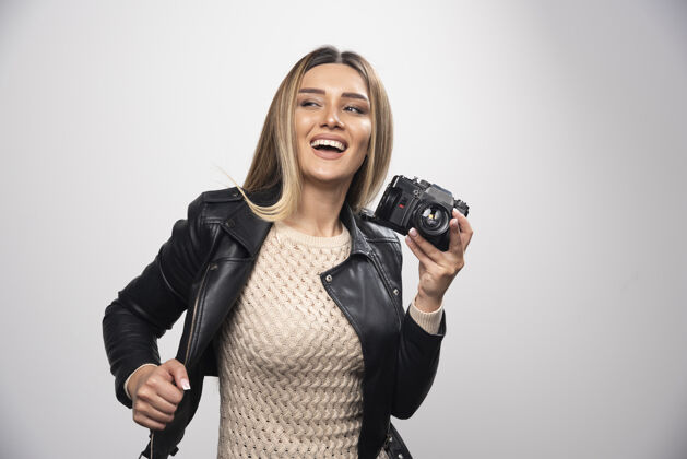 相机一位身穿黑色皮夹克的年轻女士 以积极微笑的态度用相机拍照休闲乐趣照片
