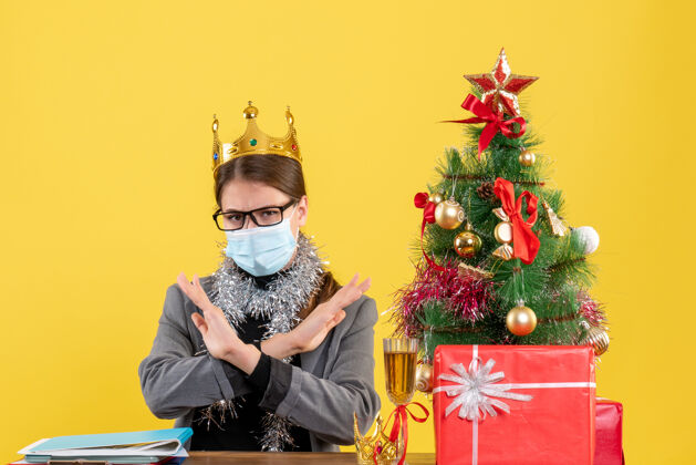 手正面图：戴着医用面罩的年轻女孩交叉双手 圣诞树和鸡尾酒礼物脖子支架医学女孩