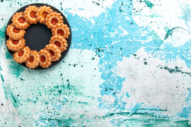 成型的俯视美味饼干圆形与果酱形成的浅蓝色背景上黑色盘子饼干糖甜饼干蛋糕顶部圆视图