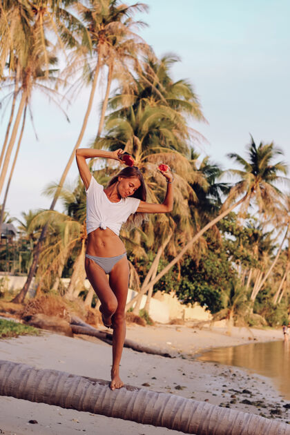 海洋日落时分 热带海滩上 一位年轻的高加索健康女士手拿西瓜身穿白色上衣和有热带水果的内裤 看起来很运动的女性明亮新鲜休息