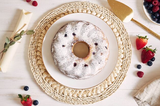 烘焙一张白色背景的白色桌子上放着水果和粉末的环形蛋糕的俯视镜头美食聚会浆果