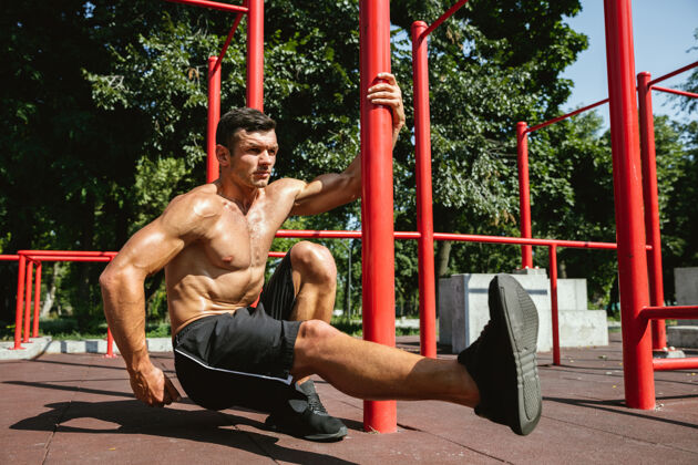 运动员年轻肌肉发达的白种人赤膊男子做蹲附近的单杠美学肌肉锻炼