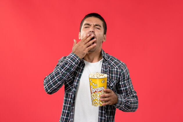 歌手正面图：年轻男子拿着爆米花包 在红墙电影院打哈欠男性年轻艺人