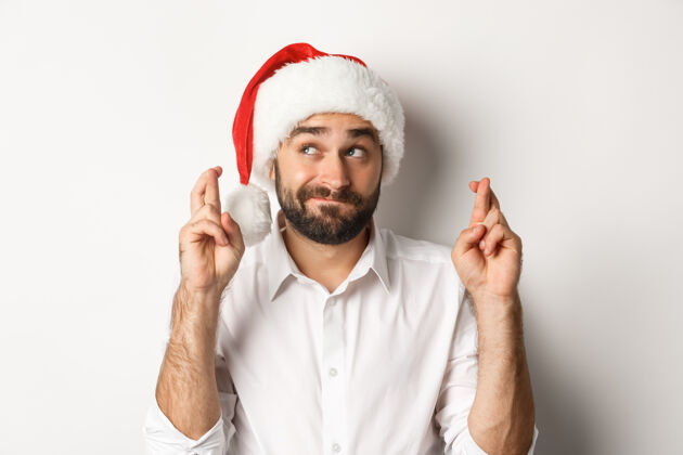 开朗派对 寒假和庆祝概念戴圣诞帽的快乐男人许下圣诞愿望 十指交叉祝好运 左上角充满希望幸福情绪化脸