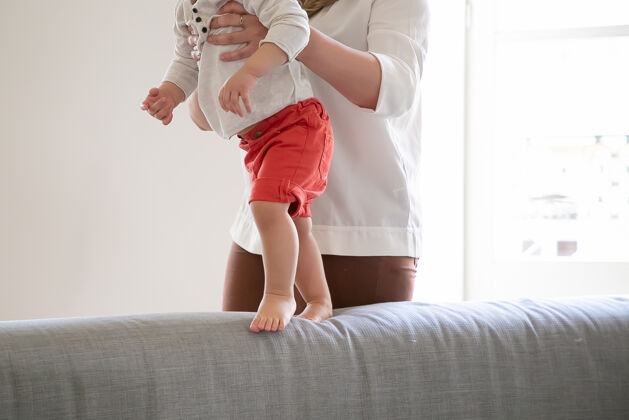 腿妈妈在家里帮助宝宝在沙发上行走孩子在妈妈的支持下迈出第一步不规则镜头亲子关系和童年概念儿童白种人肖像