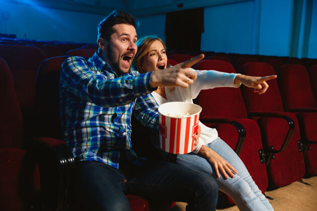 大厅迷人的年轻白种人夫妇在电影院 房子或电影院看电影看起来富于表现力 惊讶和情绪化独自坐着玩关系 爱情 家庭 周末时间电影院女人休闲