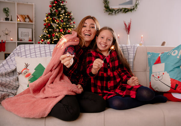 抱着笑眯眯的母女俩拿着闪闪发光的东西 裹着毯子坐在沙发上 在家里享受圣诞节时光时间火花家
