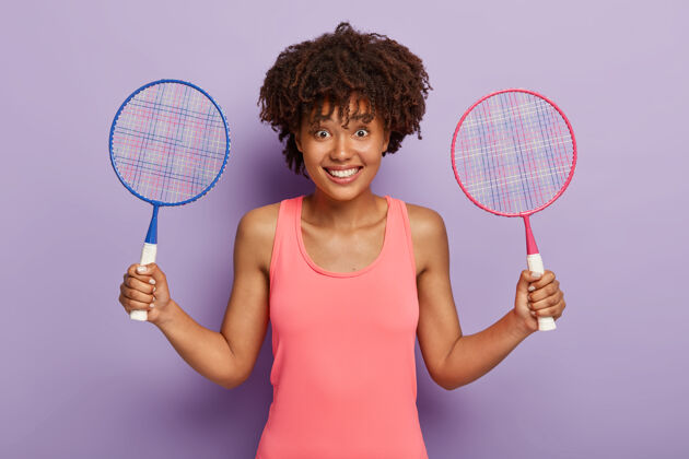 娱乐快乐的美国黑人妇女拿着两个网球拍 邀请她一起玩游戏 在网球比赛之间休息运动装比赛无忧无虑