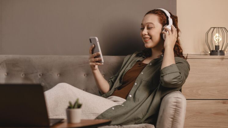 人在家沙发上用现代耳机和智能手机的女人年轻人女性个人