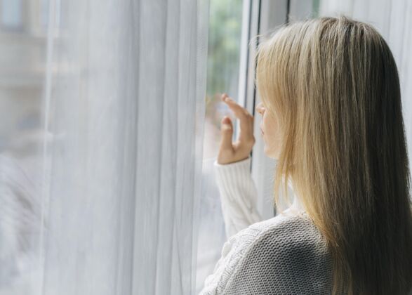 病毒大流行期间家里的女人透过窗户看预防隔离流行病