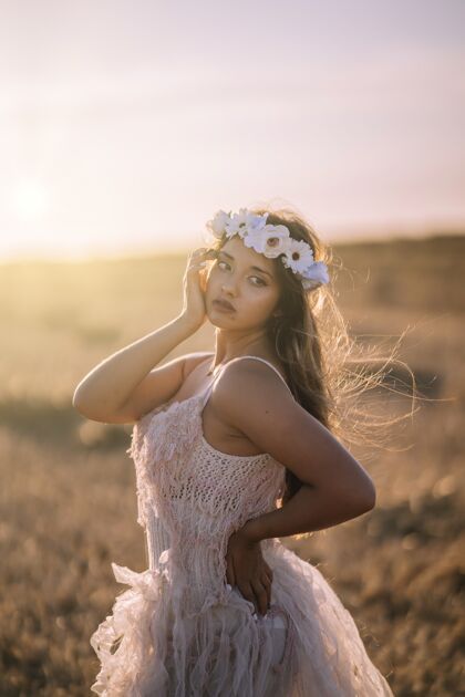 风景一个年轻的白人女性穿着白色的裙子和白色的花环摆在一个领域的垂直镜头乡村山土地