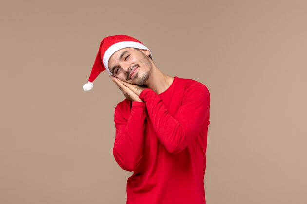 一个正面图年轻男性疲惫不堪 试图在圣诞节假期睡上一个棕色的背景成人男性前面
