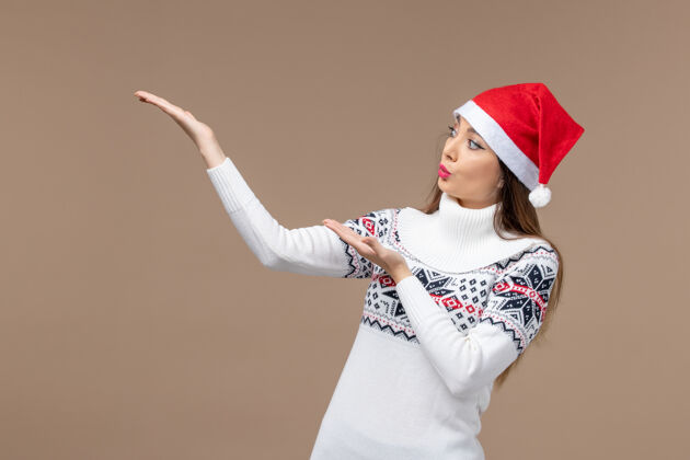 欢快正面图棕色背景上戴着红色圣诞帽的年轻女性感慨圣诞新年情感新人物