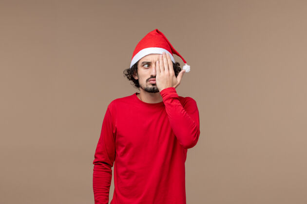 正面正面图：一个年轻人在一个棕色背景的圣诞假期里遮住了半张脸肖像情感成人