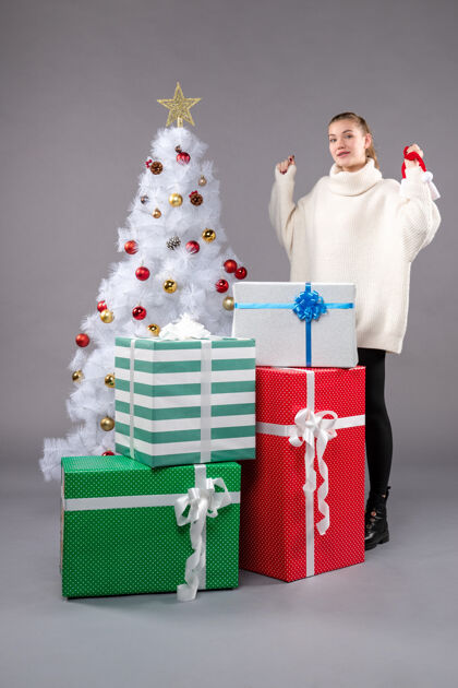圣诞帽年轻的女性在灰色的圣诞礼物周围圣诞老人人礼物