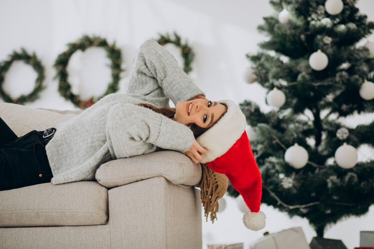 礼物坐在圣诞树旁沙发上的年轻女子圣诞老人美丽装饰
