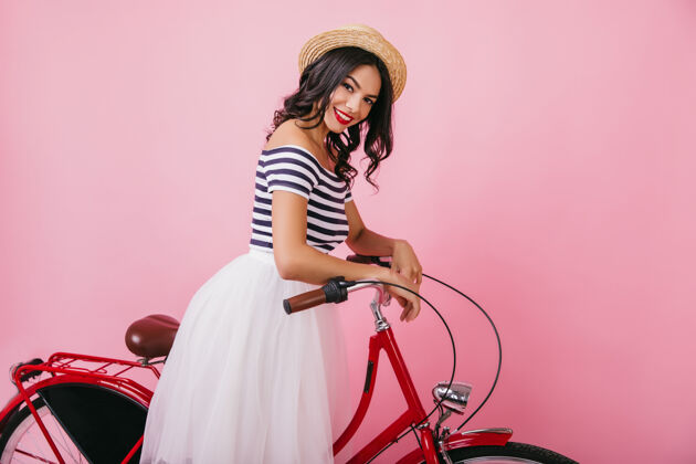 人迷人的年轻女士 卷发 摆着红色的自行车 笑着室内拍摄可爱的拉丁女人戴着优雅的草帽美丽夏天复古