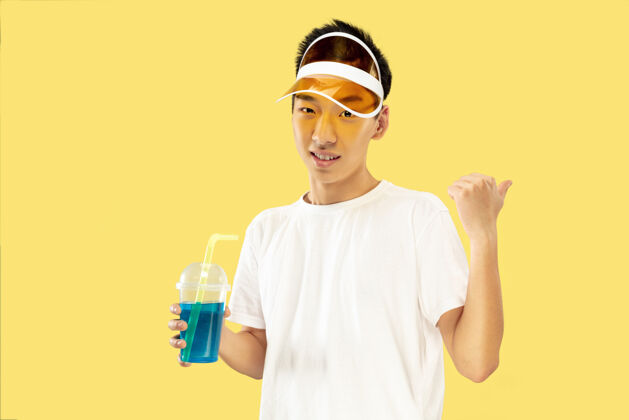 惊奇韩国年轻人的肖像穿白衬衫 戴黄帽子的男模喝鸡尾酒人类情感的概念 表达 夏天 假期 周末情感惊奇周末