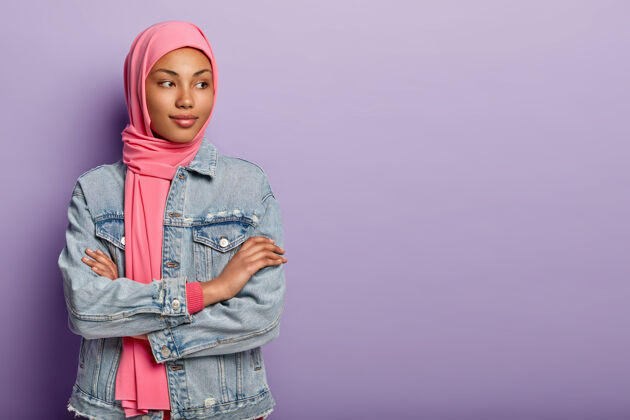 体贴室内镜头体贴美丽的阿拉伯女性双手交叉站在室内 注意力不集中 思考未来的计划 戴着头巾和牛仔外套 隔离在紫色的墙上个性自由空间头像