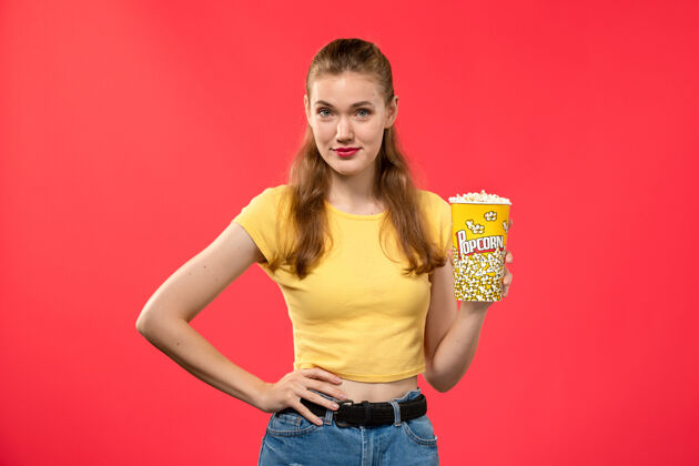 电影院正面图年轻女性在电影院拿着爆米花包 摆姿势在红墙电影院的女性趣味电影爆米花电影年轻